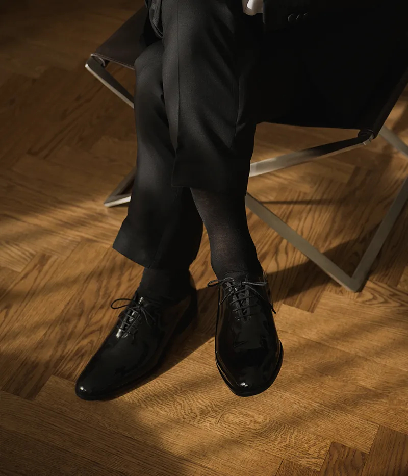 One man sitting in a chair wearing his Loake shoes. Shoes shown are Regal in Black patent leather