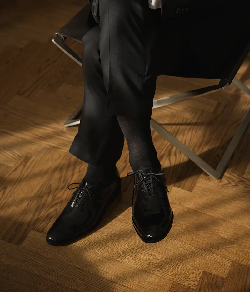 One man sitting in a chair wearing his Loake shoes, getting ready for a wedding or a christmas party. Shoes shown are Regal in Black patent leather