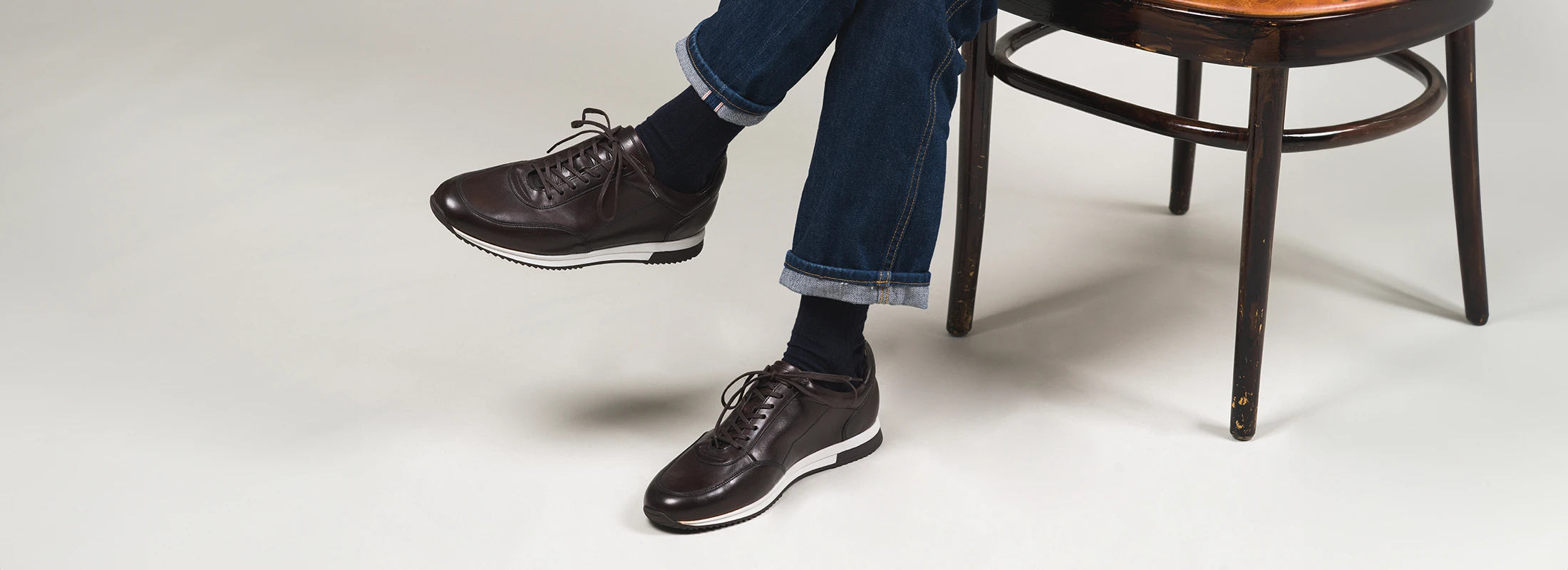 Man sitting wearing a pair of Loake Bannister Trainers in Dark Brown Calf Leather