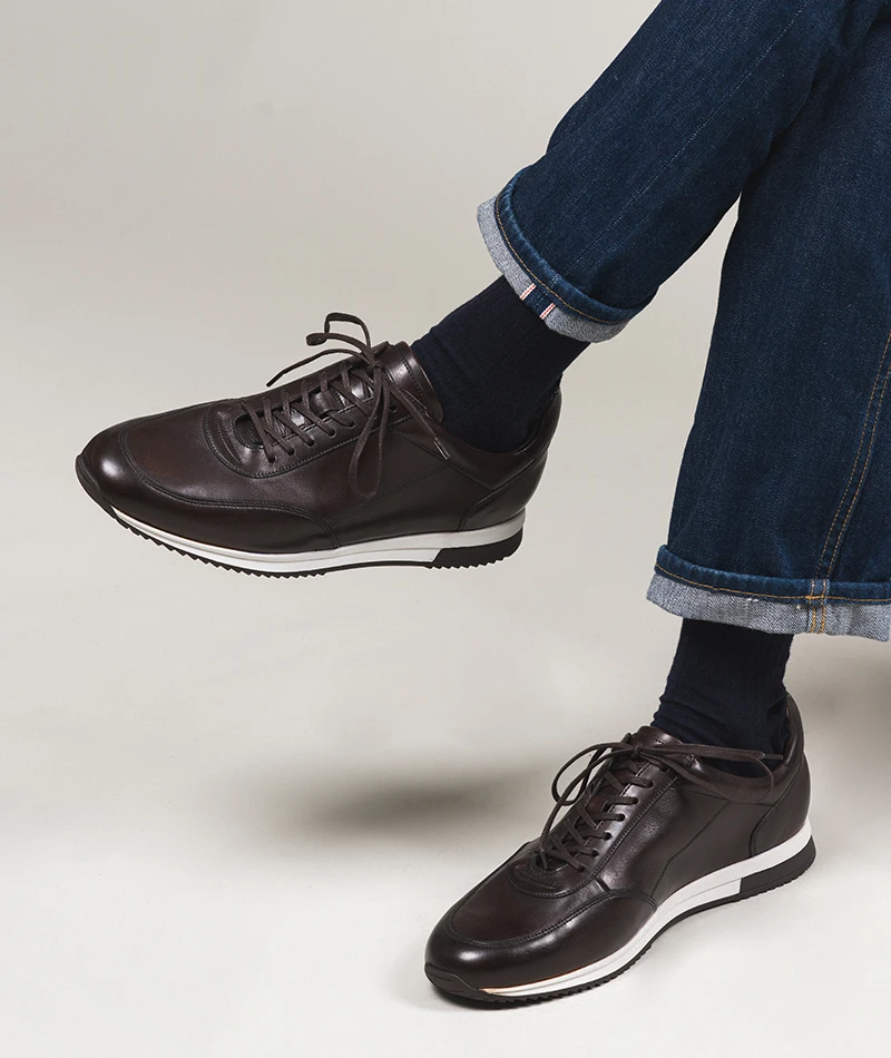 Man sitting wearing a pair of Loake Bannister Trainers in Dark Brown Calf Leather