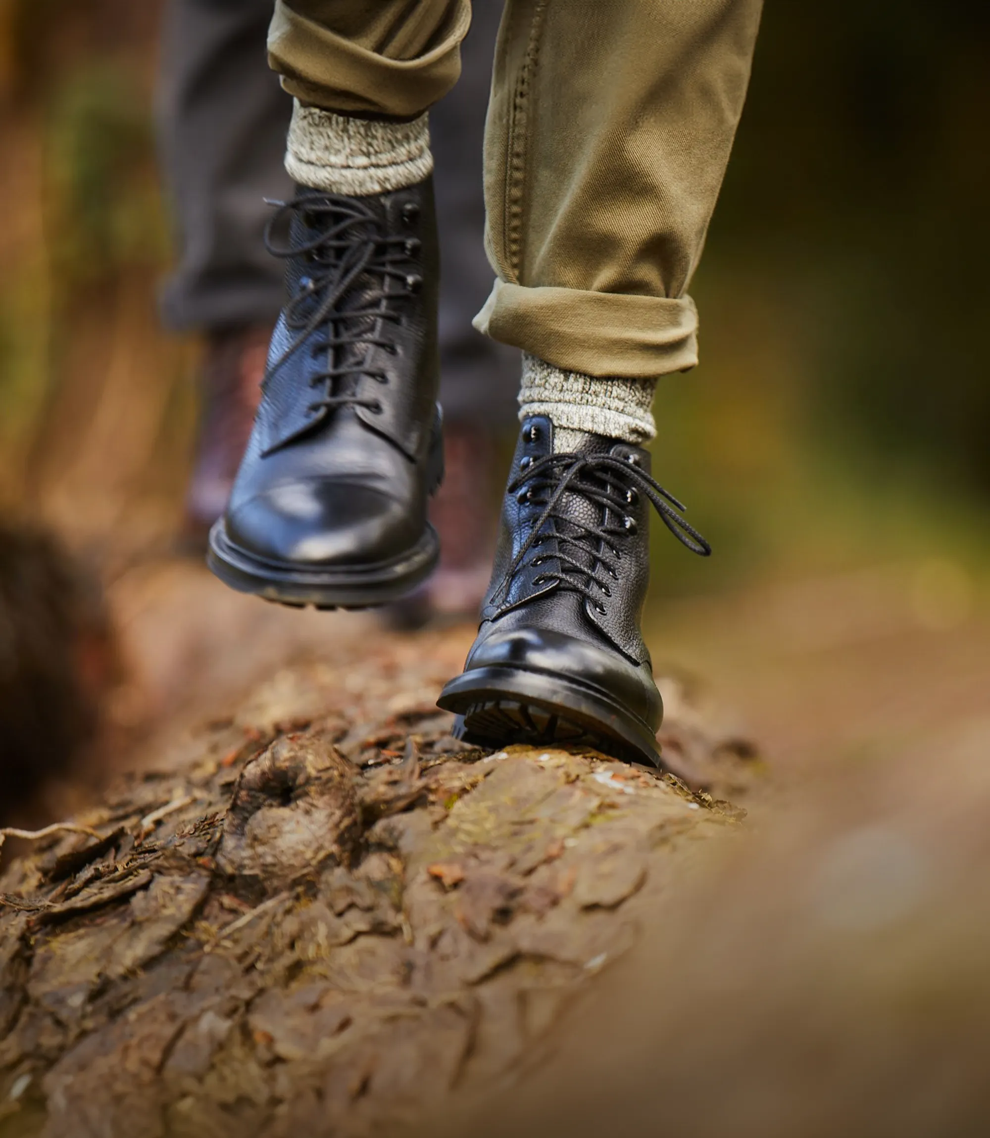 Man walking along a fallen tree trunk, wearing rolled up khaki trousers and their Loake Sedbergh country boots in Black Grain Calf leather