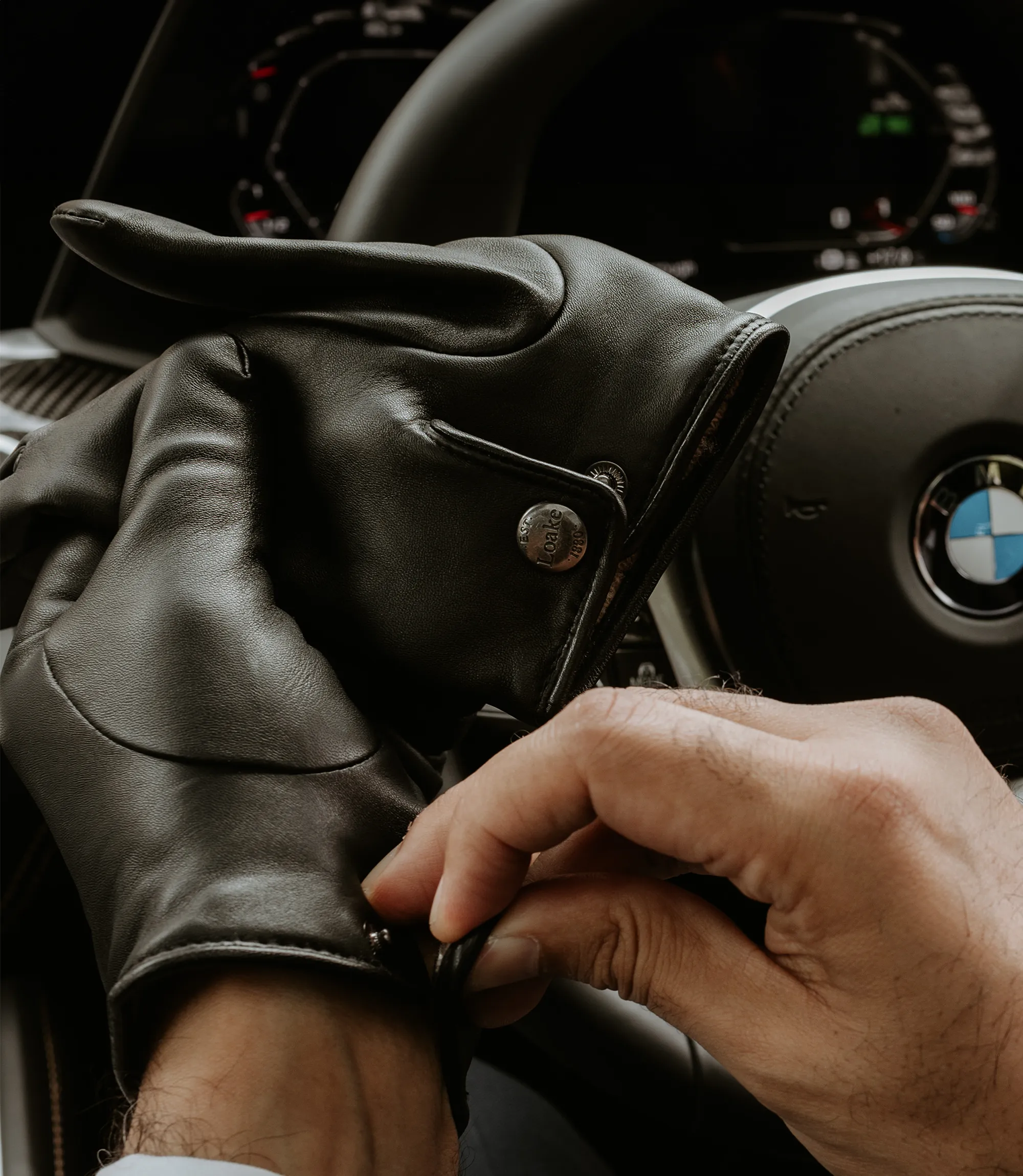 A man sitting in his car whilst putting on his black leather Shackleton gloves by Loake Shoemakers
