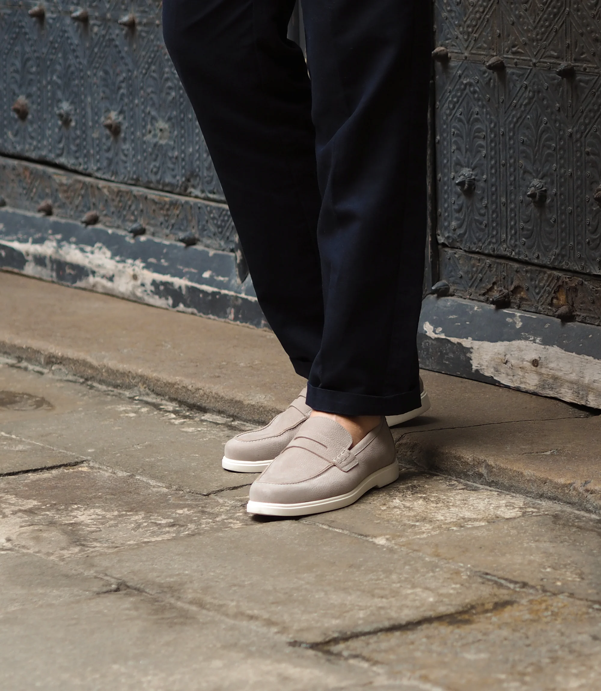 A man wearing navy blue trousers standing on concrete floor, wearing Loake Como Loafers in Grey Nubuck.