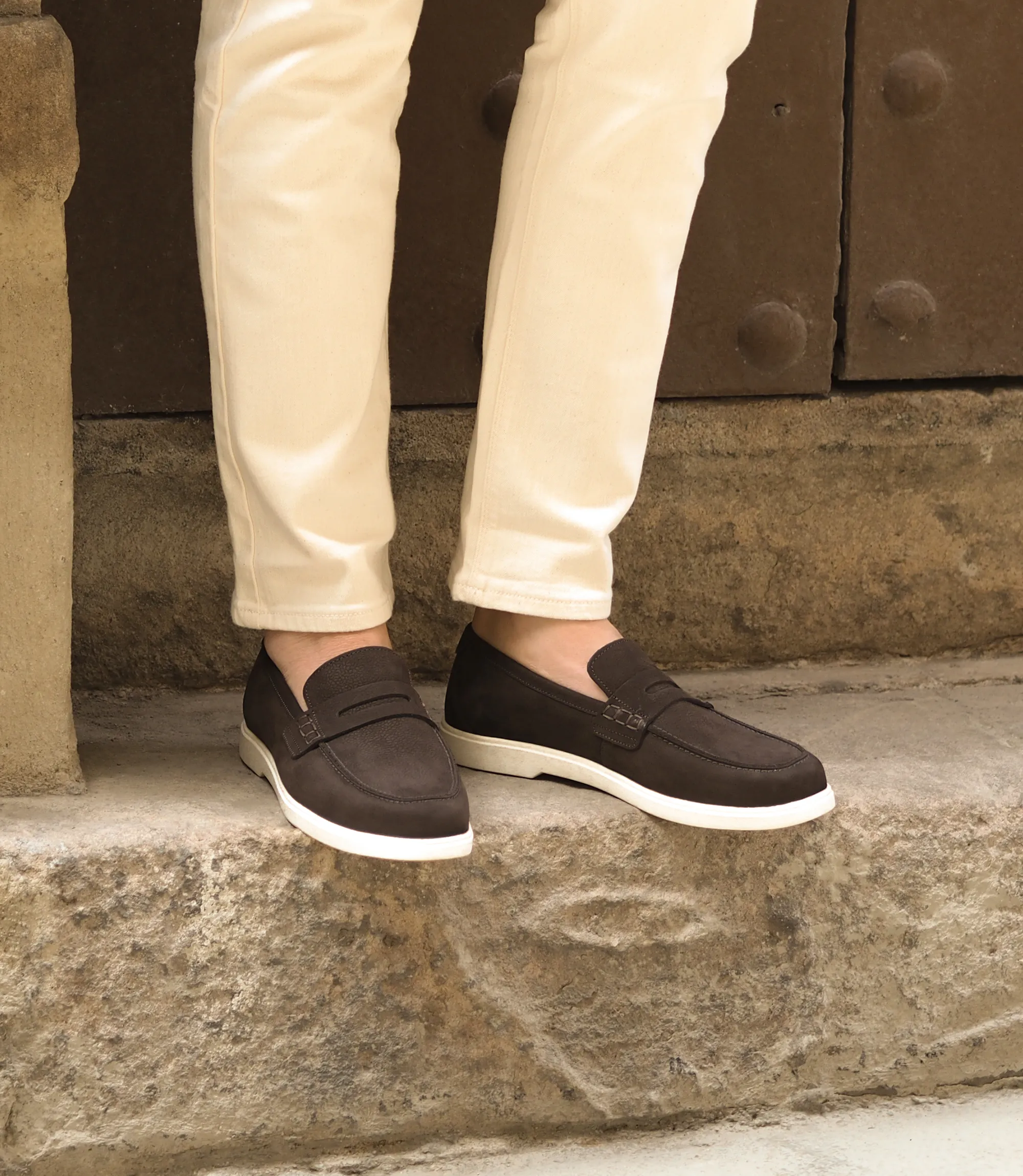 Man standing on a stone step in a warm city location, whilst wearing his Loake Como Loafer Shoes in Dark brown Nubuck
