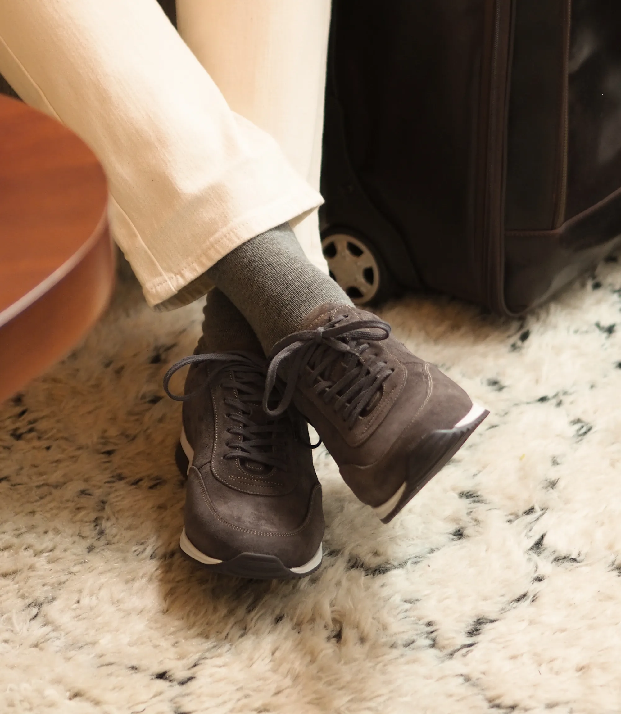 Man sitting in his holiday hotel in cream chinos and wearing his Loake Bannister trainers in Anthracite Suede.