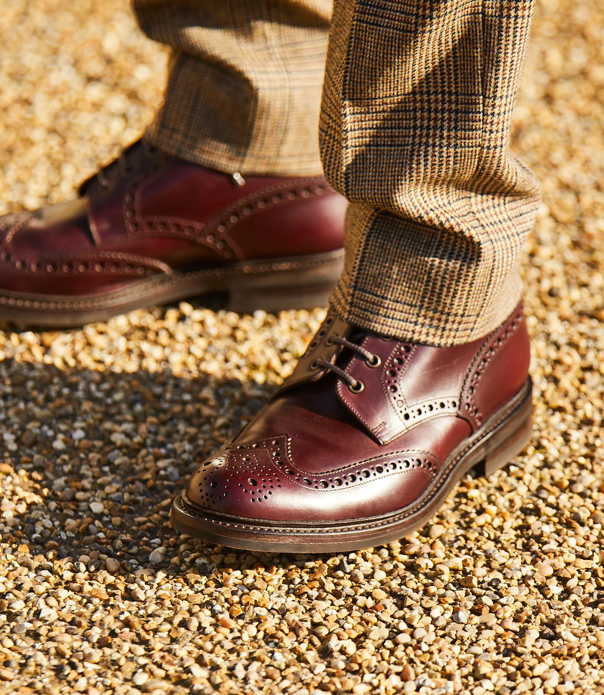 A man wearing brown chequered trousers standing outside wearing his Loake Bedale Boots in Burgundy Leather.