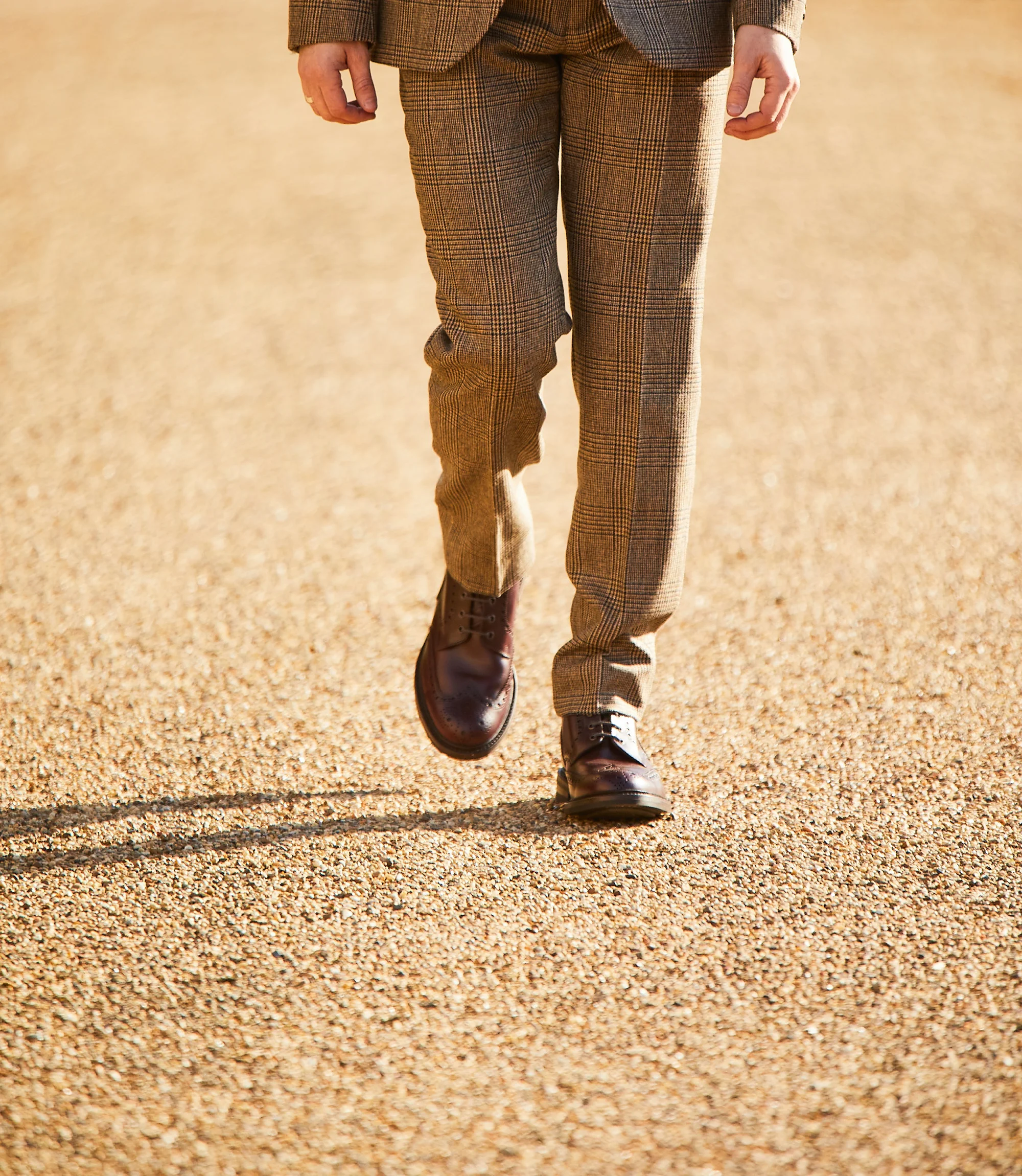 A man wearing brown chequered trousers standing outside wearing his Loake Bedale Boots in Burgundy Leather.