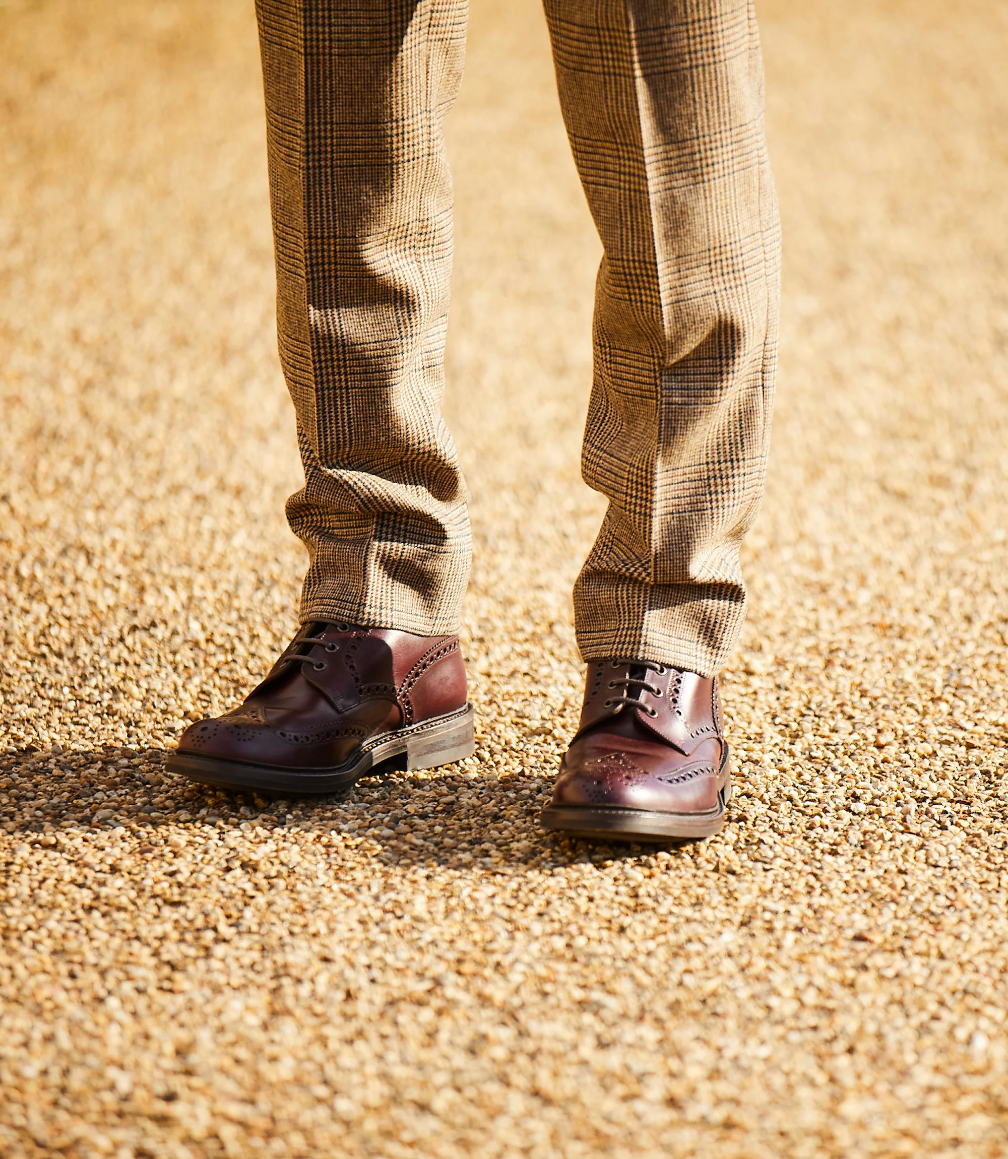 A man wearing brown chequered trousers standing outside wearing his Loake Bedale Boots in Burgundy Leather.
