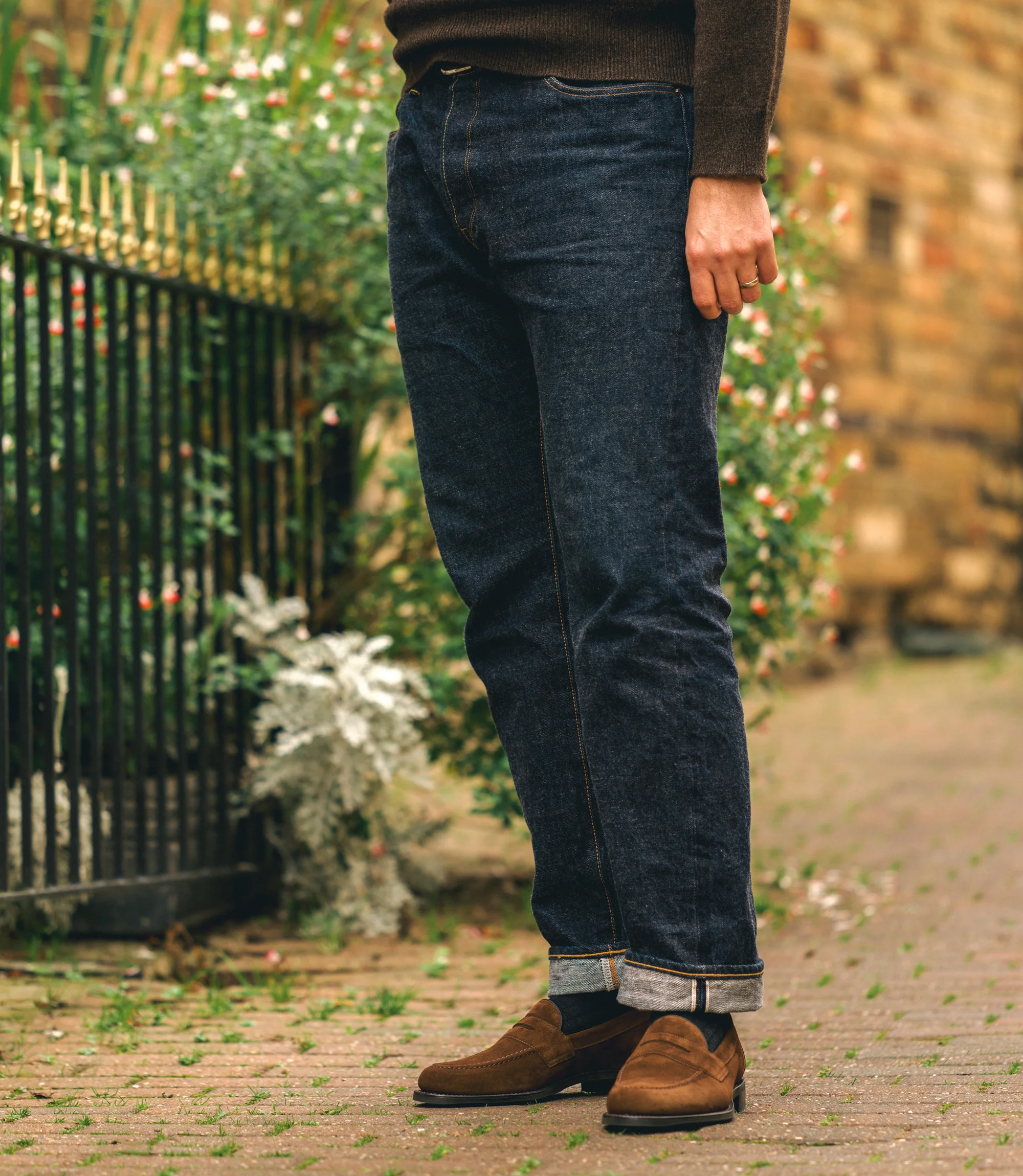 A man wearing blue denim trousers standing on a cobbled floor wearing his Loake Imperial Loafers in brown Suede.