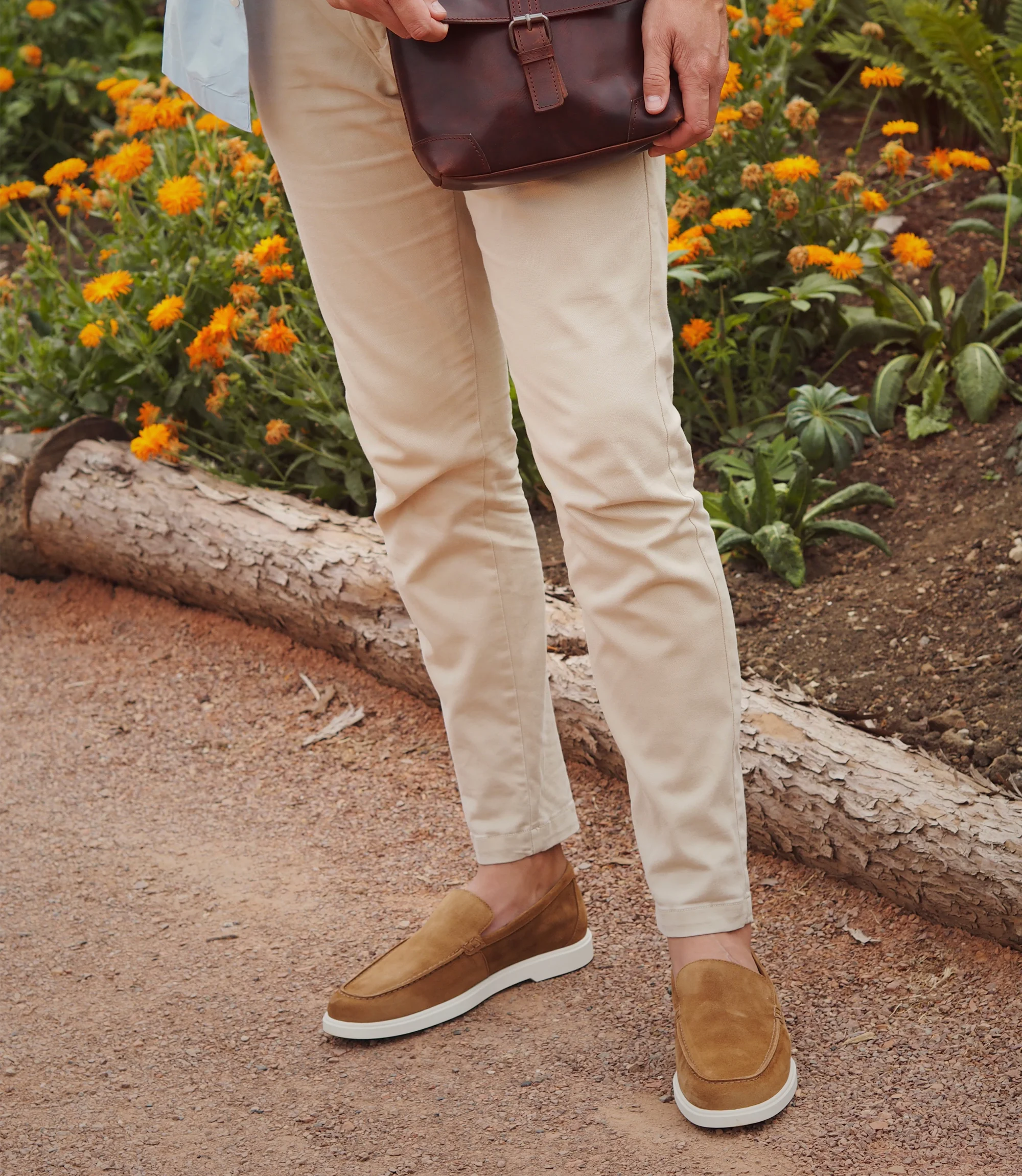 A man wearing beige trousers holding a brown bag standing outside wearing his Loake Tuscany Loafers in Brown Suede.