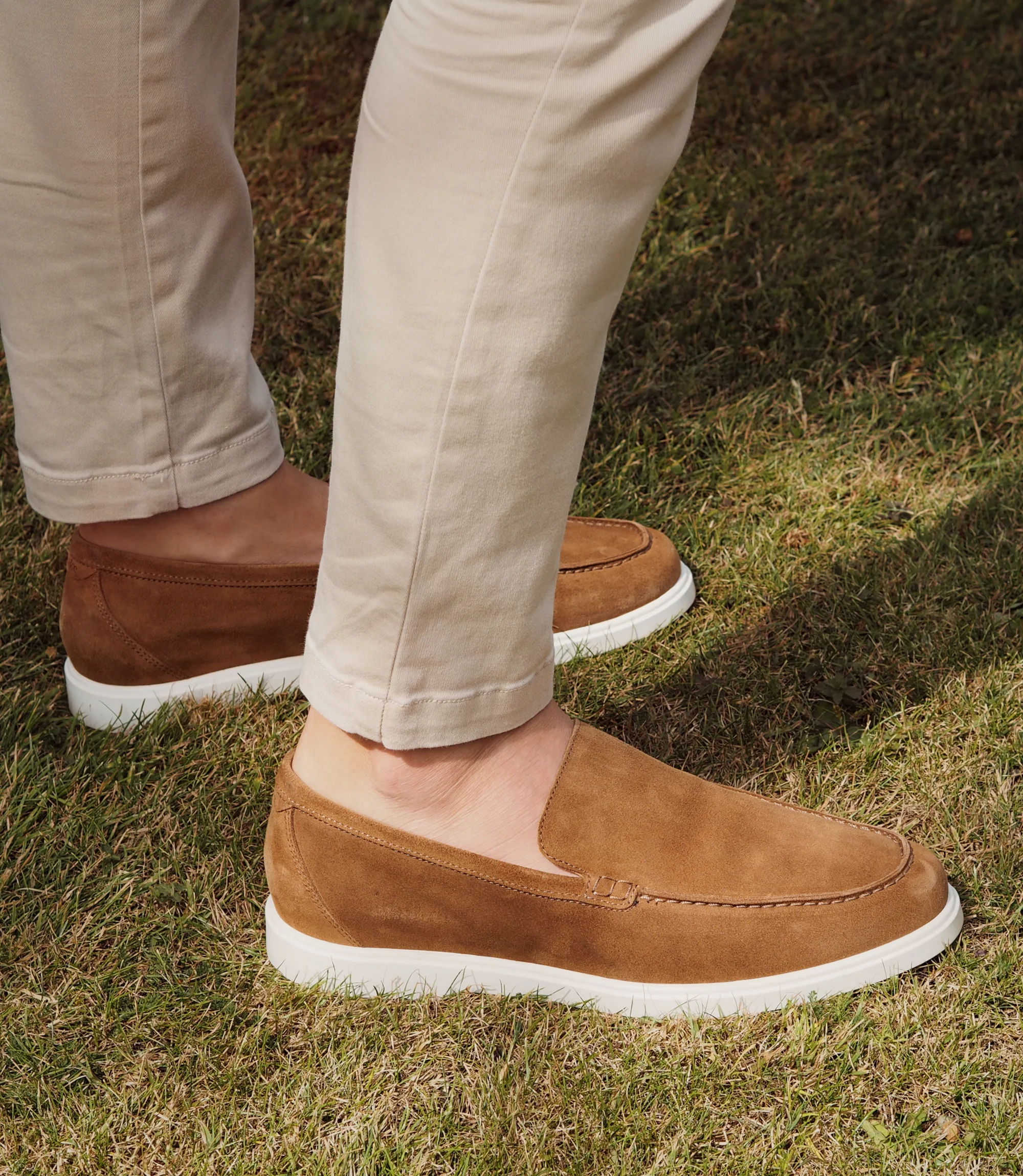 A man wearing beige trousers standing outside on grass wearing his Loake Tuscany Loafers in Brown Suede.