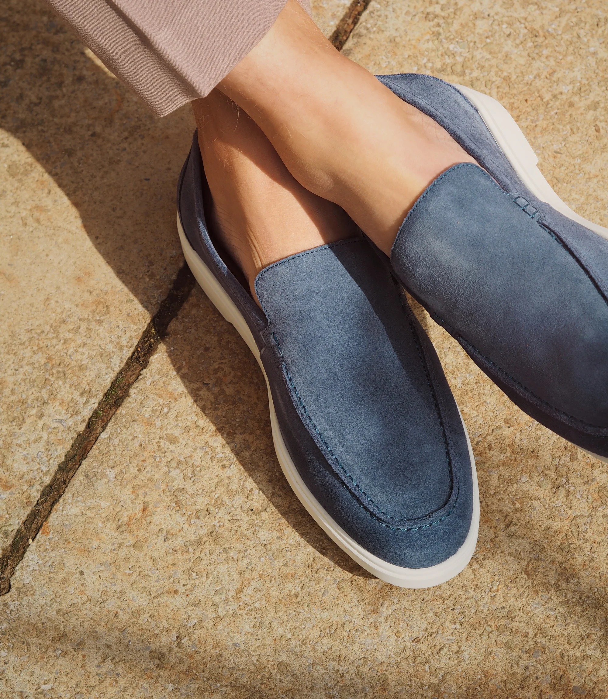 A man sitting down legs crossed on a chair in brown trousers wearing his Loake Tuscany Loafers in Light Blue Suede.