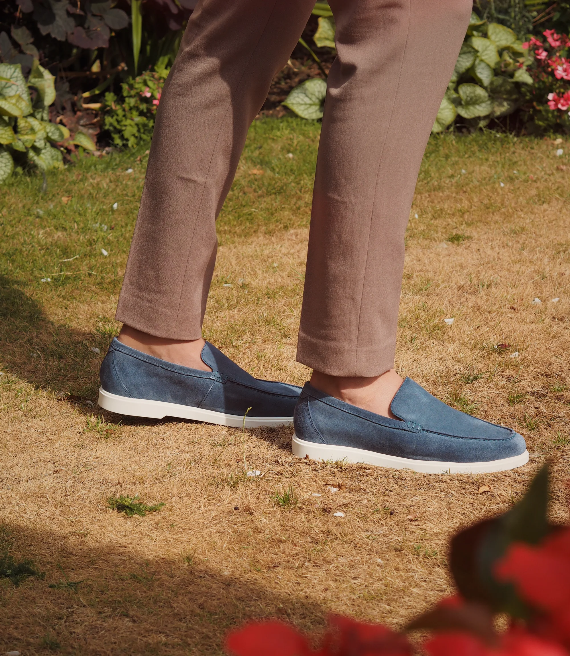 A man wearing brown trousers standing outside on grass wearing his Loake Tuscany Loafers in Light Blue Suede.