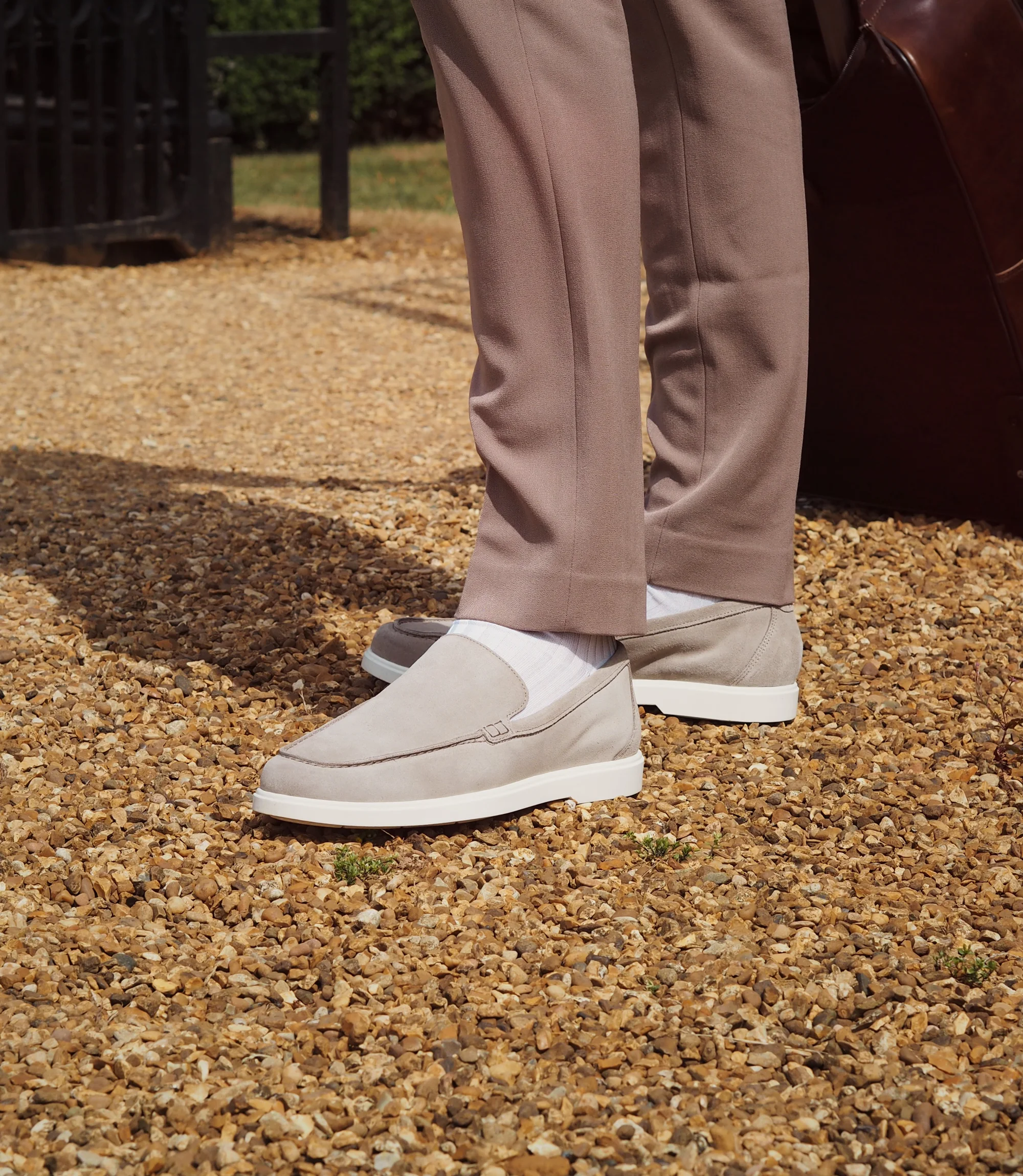 A man wearing brown trousers standing outside on stones wearing his Loake Tuscany Loafers in Stone Suede.