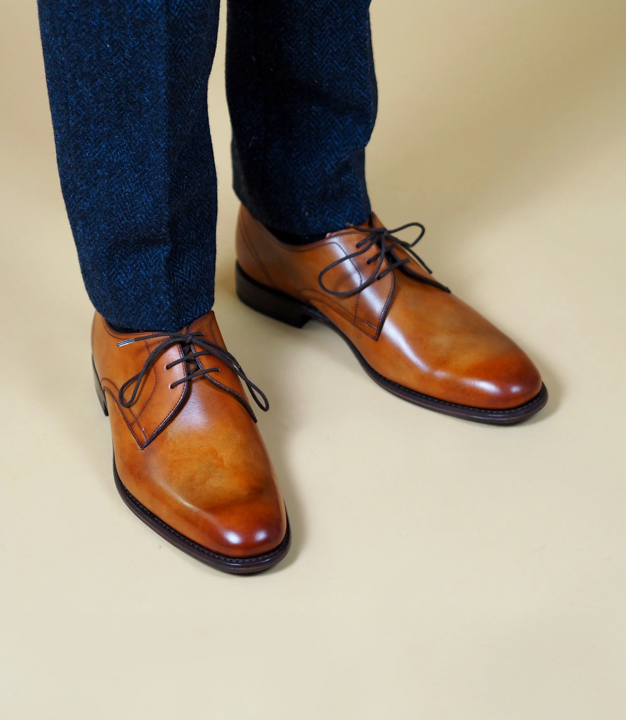 A man standing in a studio backdrop wearing navy trousers wearing his Loake Atherton in Tan leather.