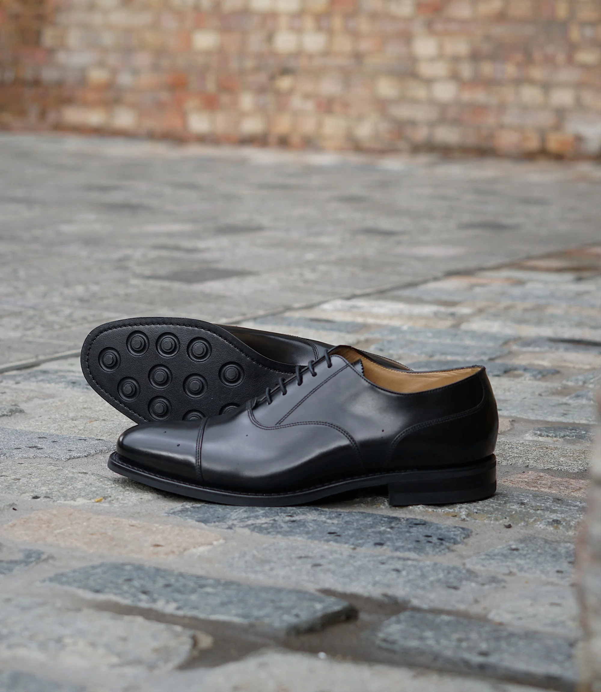 A pair of Loake 300 in Black Leather placed outside on concrete floor separately.