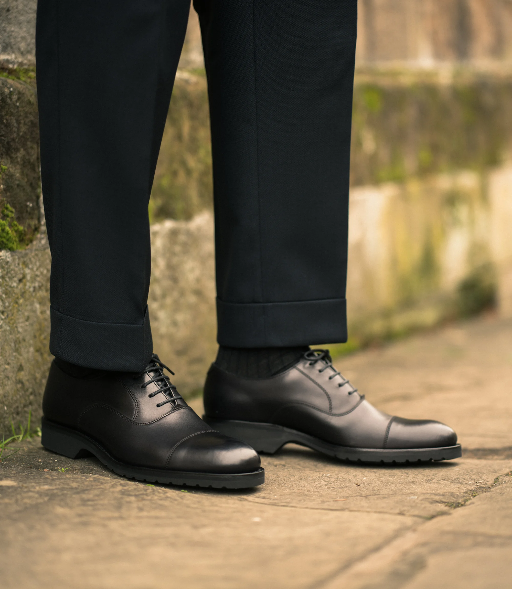 A man wearing navy trousers standing on concrete floor outside wearing his Loake Hitchcock in Black Leather.