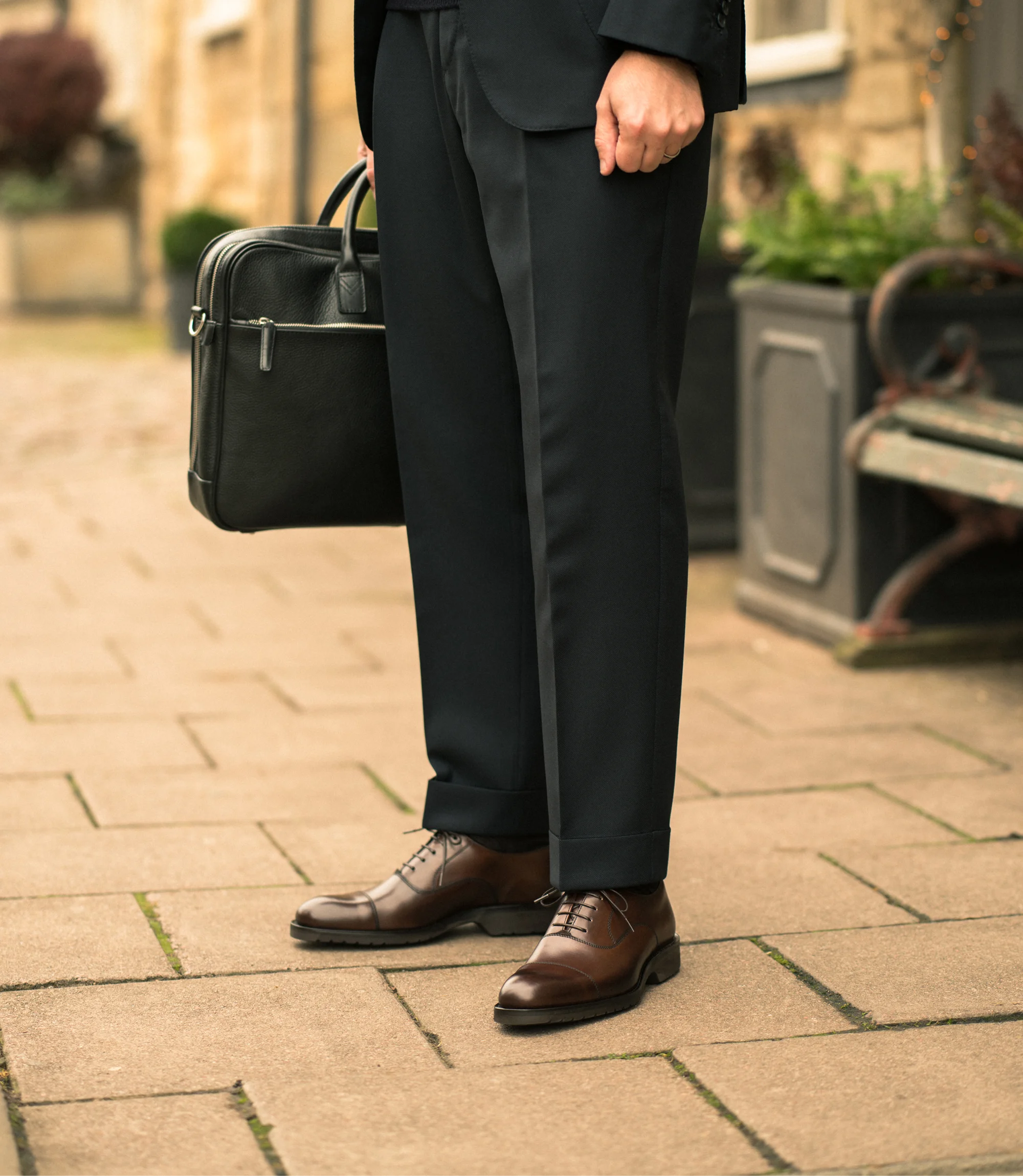 A man standing with a Loake Westminster Briefcase in a black suite wearing his Loake Hitchcock in Dark Brown Leather.