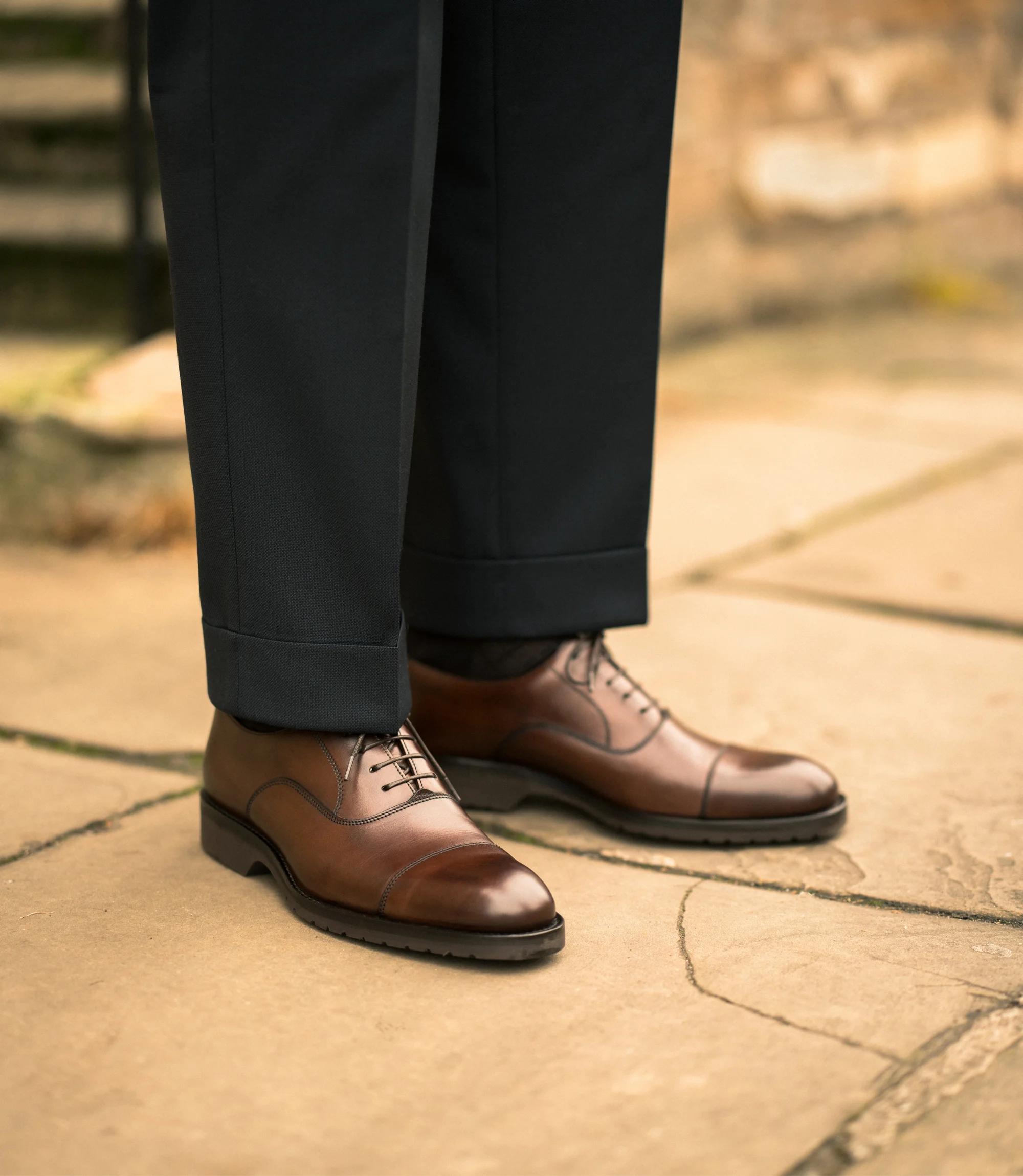 A man wearing black trousers standing outside on concrete floor wearing his Loake Hitchcock in Dark Brown Leather.