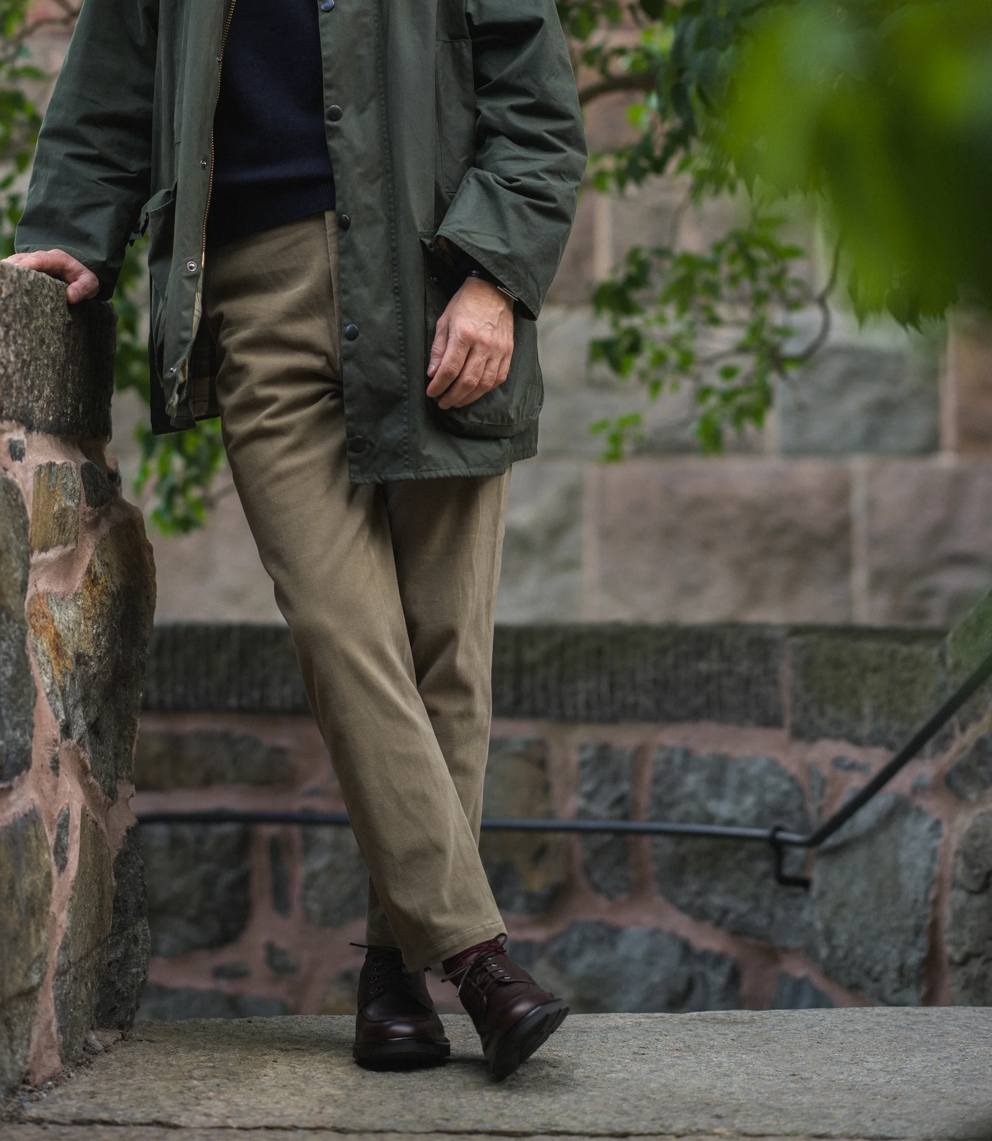 A man wearing beige trousers and green coat standing outside near steps wearing his Loake Mowbury in Dark Brown leather.