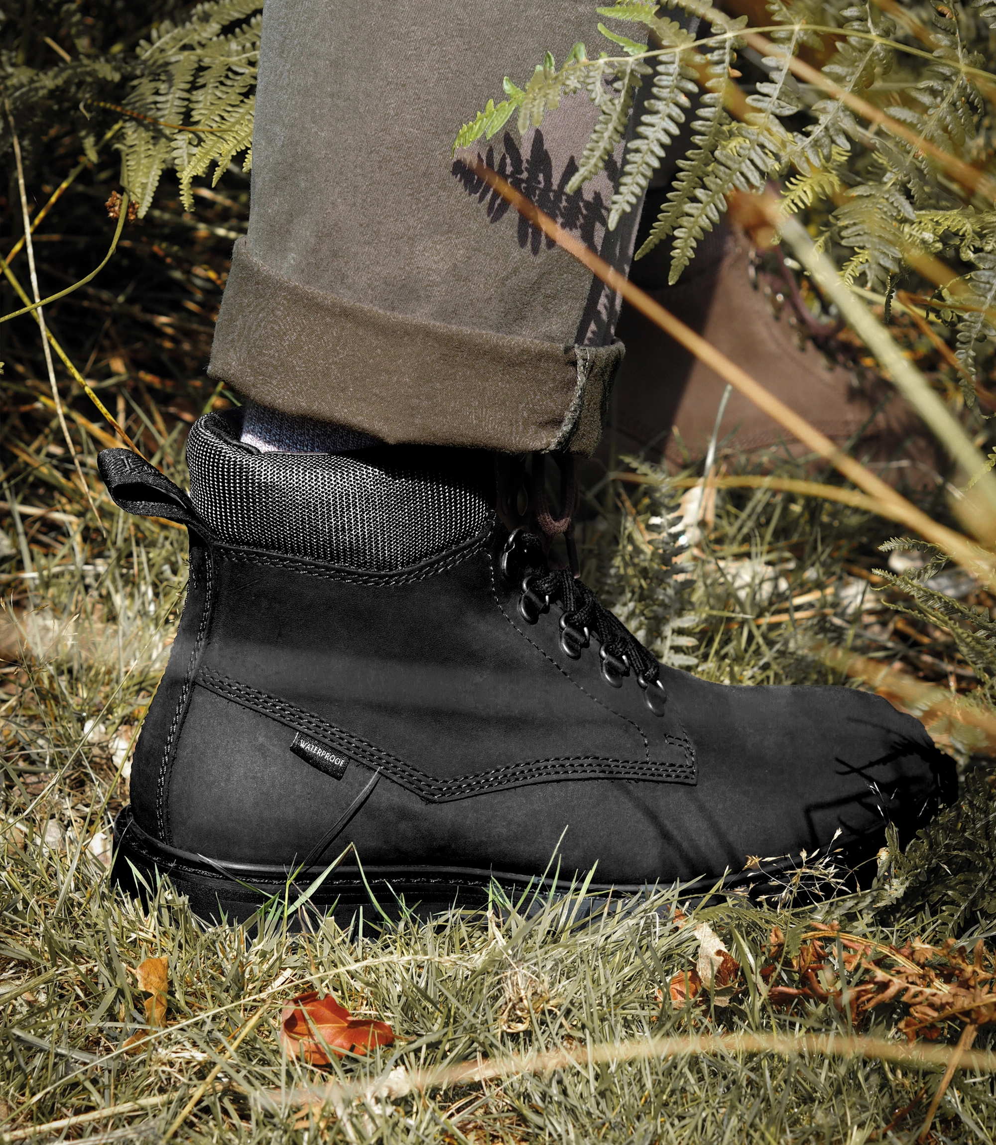 A man wearing green trousers, wearing his waterproof Loake Nevis Derby Boots. He is standing on grass outside in an English countryside. Boots shown are Nevis in Black Oiled Nubuck leather.