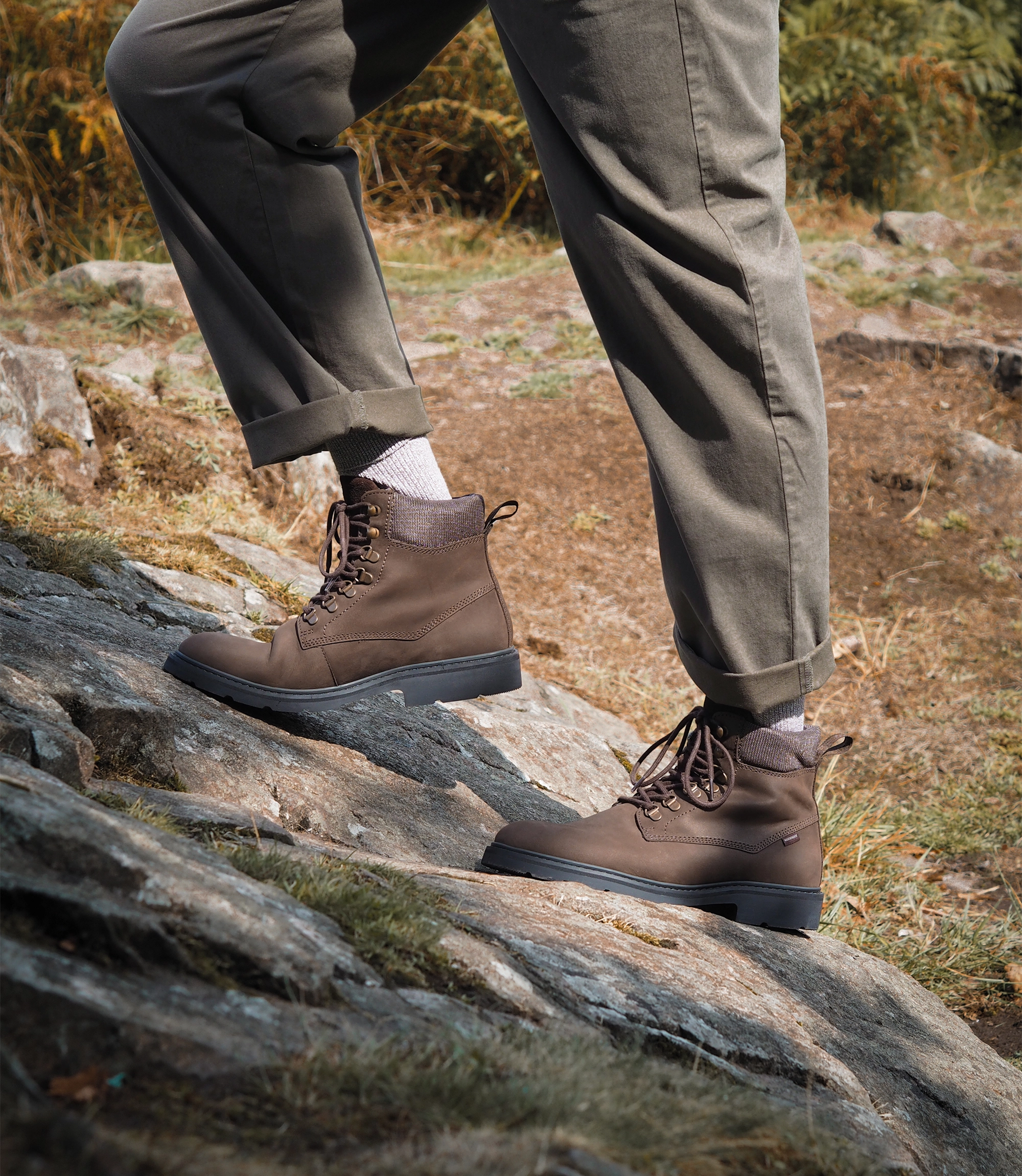 A man wearing olive green trousers, brown waxy country jacket and his waterproof Loake Nevis Derby Boots. He is walking through a forest in an English country village. Boots shown are Nevis in Brown Oiled Nubuck leather