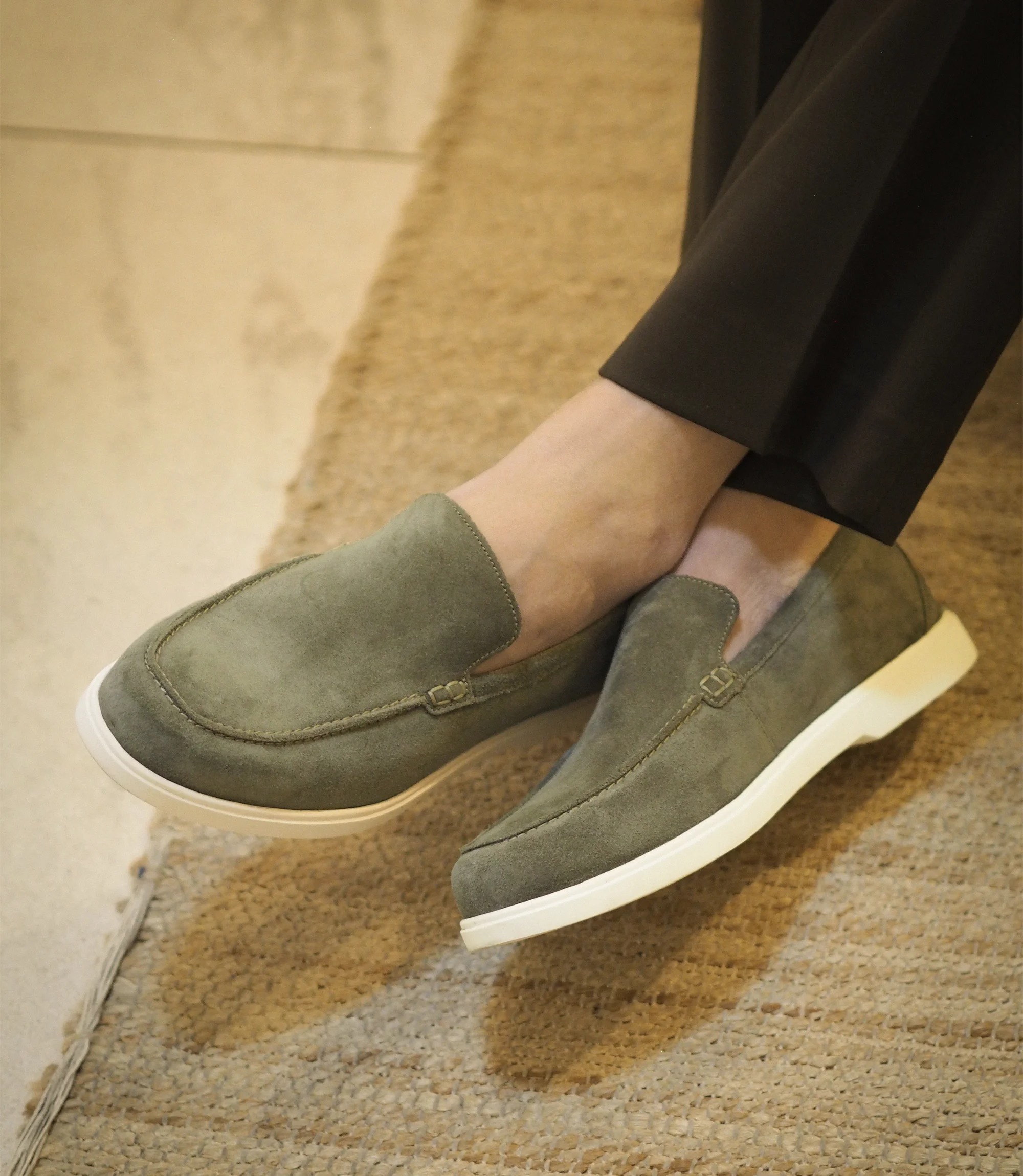 A man sitting down on a chair wearing brown smart trousers crossed legs wearing his Loake Tuscany Loafers in Olive Suede.