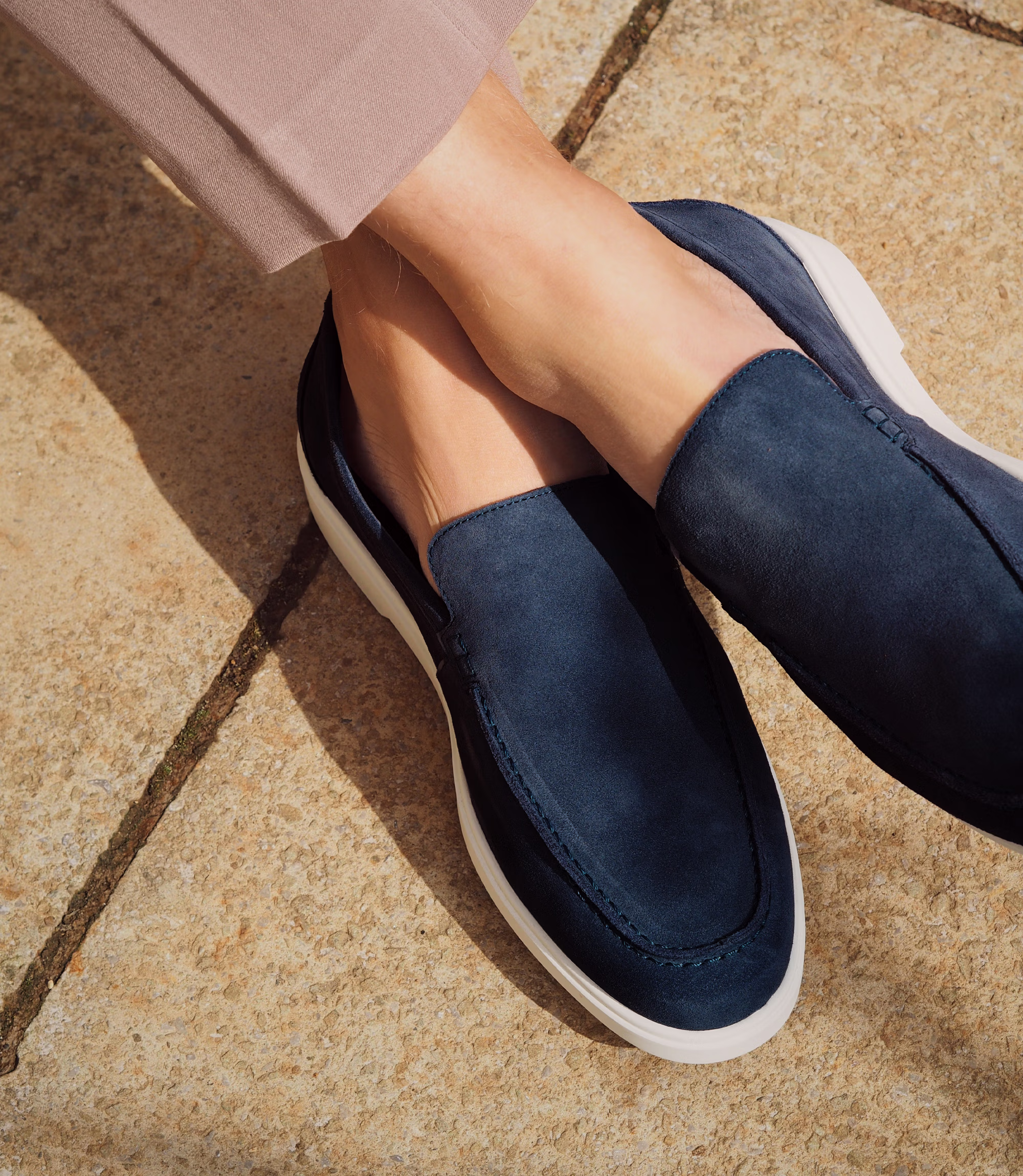 A man sitting down legs crossed on a chair in brown trousers wearing his Loake Tuscany Loafers in Navy Suede.