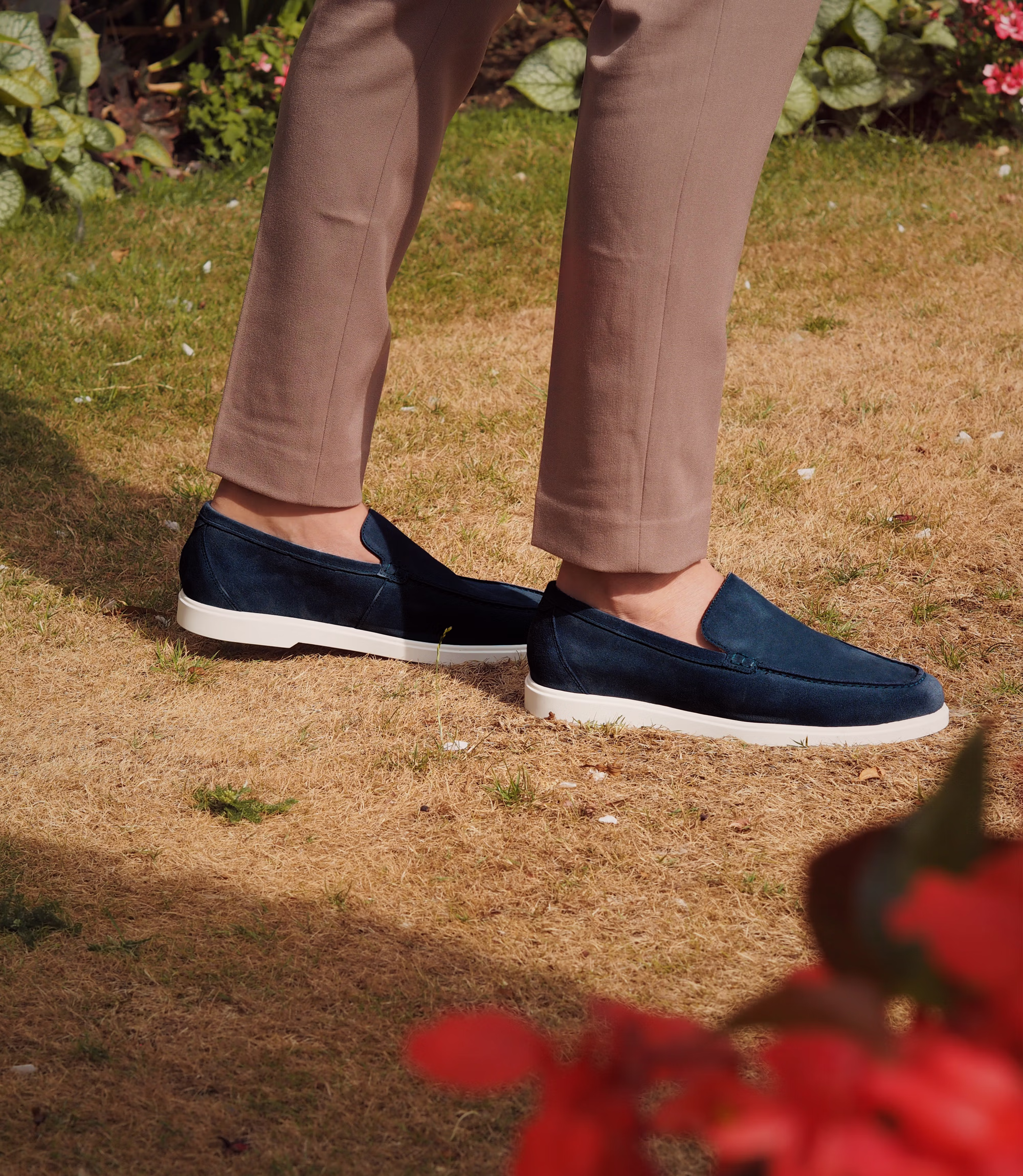 A man wearing brown trousers standing outside on grass wearing his Loake Tuscany Loafers in Navy Suede.